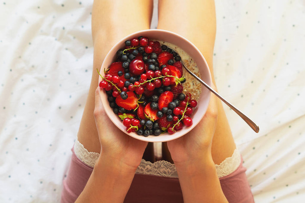 Healthy summer breakfast in the bed. Woman eating oatmeal porridge with berries. Healthy eating concept. Top view - Fotografie, Obrázek