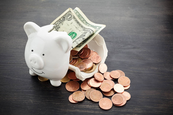 Broken piggy bank with money on dark wooden background - Фото, изображение