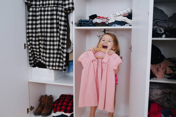Portrait of little girl in new pink overalls playing inside of open wardrobe - Fotoğraf, Görsel