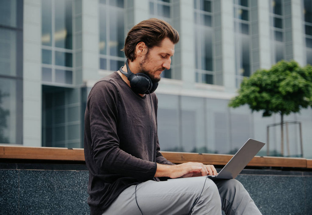 Freelancer Man in the big urban city working with a laptop phone camera and listening music via headphones - Фото, зображення