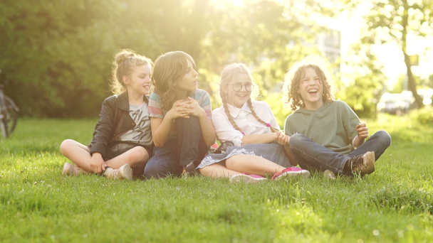 Красивые школьники, мальчики и девочки смеются сидя на траве во время школьного перерыва. Возвращаясь в школу, группа подростков на пикнике. Солнечные лучи
 - Кадры, видео