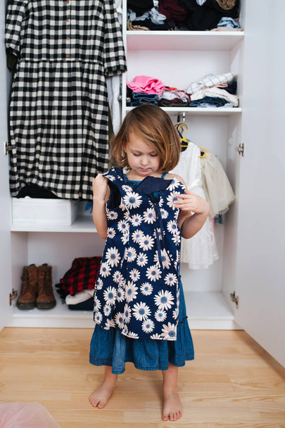 Little girl is trying on new dress in front of open wardrobe full of clothes - Fotoğraf, Görsel