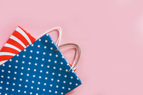 4th July holiday shopping concept. Shopping bags in national american colors  over light pink background - Foto, Imagem