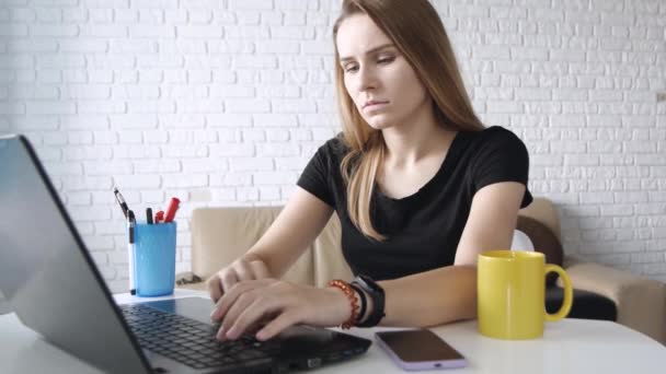 Κουρασμένη εργασία γυναίκα χρησιμοποιεί το laptop της, πληκτρολογώντας ενώ κάθονται στην επιφάνεια εργασίας πάνω από τούβλα τοίχο, βαριεστημένη πρόσωπο. Κλείσε το πορτρέτο. Έννοια ανεξάρτητη εργασία, επιχείρηση, επικοινωνία, σπουδές. - Πλάνα, βίντεο
