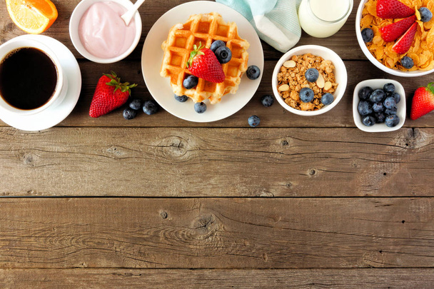 Comida de desayuno frontera superior. Frutas, cereales, gofres, yogur y café. Vista superior sobre un fondo de madera oscura con espacio para copiar
. - Foto, Imagen