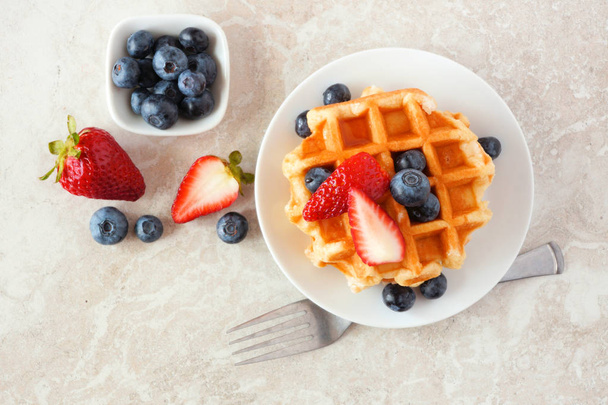 Ontbijt wafels met aardbeien en bosbessen. Top uitzicht over een heldere stenen achtergrond. - Foto, afbeelding