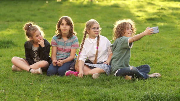 Děti ze školy sedí na trávě během školního přestávky. Spolužáci mají v parku selu. - Záběry, video