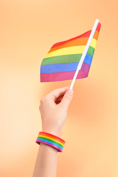Bandera LGBT en mano de mujer sobre fondo naranja. Copiar espacio
.  - Foto, Imagen