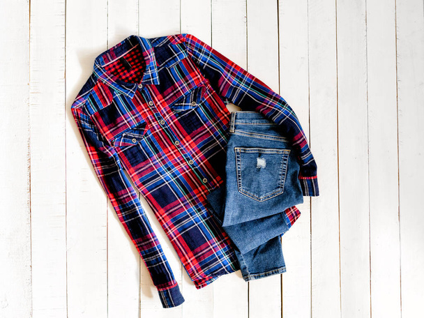 Clothes concept. Checkered shirt and jeans on wooden background. Top view - Photo, Image