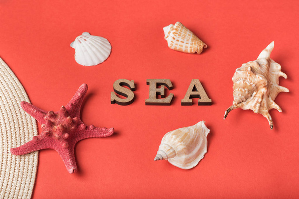 Słowo morze z drewnianych liter. Muszle, rozgwiazdy i część kapelusza. Żywe koralowe tło. Koncepcja morska - Zdjęcie, obraz
