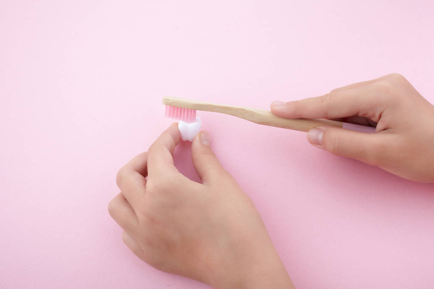 childs hand with toothbrush and white platic tooth on pink background - Foto, Imagem
