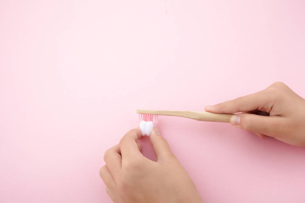 childs hand with toothbrush and white platic tooth on pink background - Valokuva, kuva