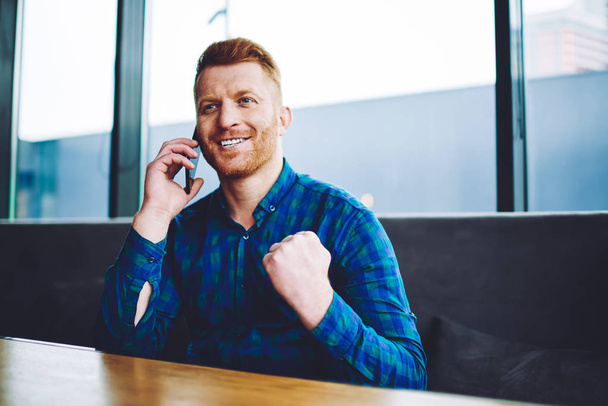 Overjoyed hipster guy feeling happy from received news about 4g connection in roaming using mobile application for communication indoors, excited man with expression making positive cellular call - 写真・画像