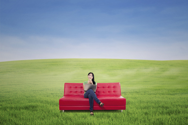 Mujer pensativa tomando café en el sofá rojo al aire libre
 - Foto, Imagen