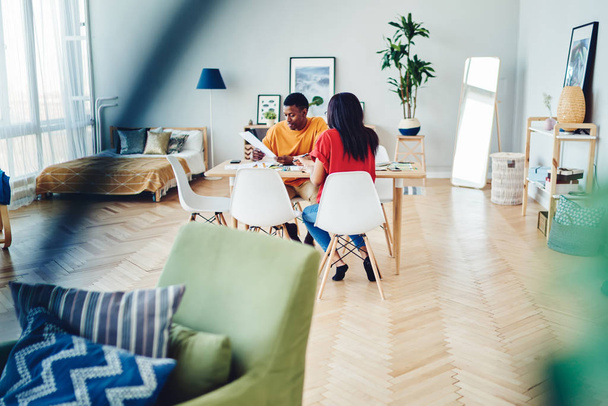African American couple sitting at table with documents and talking about family budget, dark skinned woman and man spending time in modern apartment discussing plans and creative ideas for home - Foto, Bild
