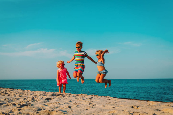 Ευτυχισμένα παιδιά άλμα στην παραλία, αγόρι και κορίτσια που διασκεδάζουν στη θάλασσα - Φωτογραφία, εικόνα