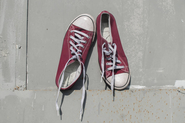 Pair of worn out vintage red old canvas sneakers on grey painted tin surface background - Photo, Image