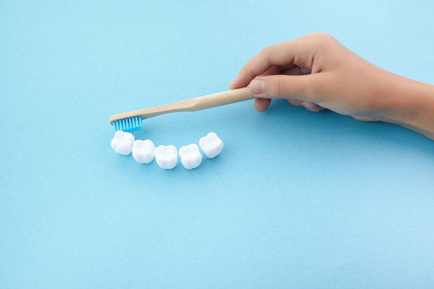 mão crianças com escova de dentes e dente branco plático no fundo azul
 - Foto, Imagem