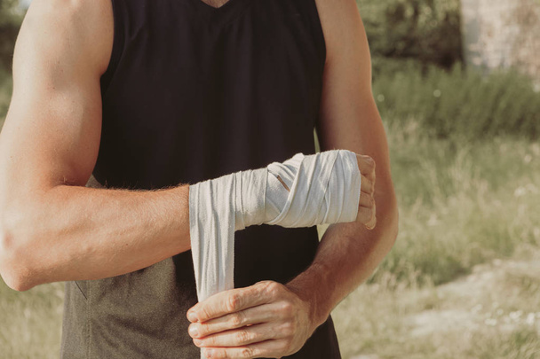 ένας αθλητής προετοιμάζεται για εκπαίδευση τυλίγοντας τα χέρια του με επίδεσμο πυγμαχίας - Φωτογραφία, εικόνα