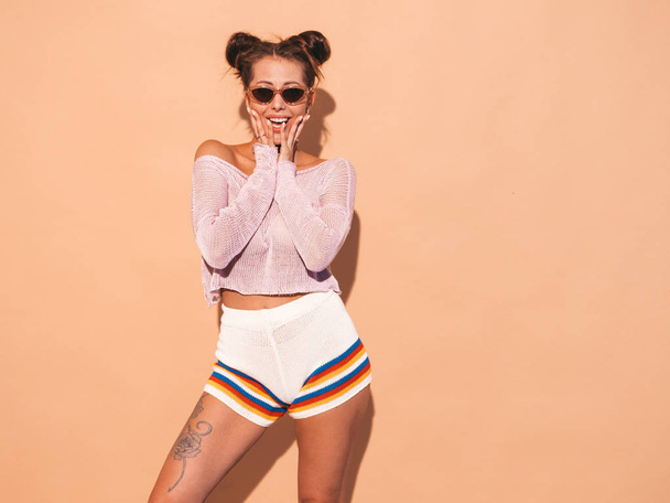 Portrait of young beautiful sexy woman with two horns hairstyle. Trendy girl in casual summer hipster knitted cardigan topic ,shorts in sunglasses. Shocked and surprised with hands near face - Foto, immagini
