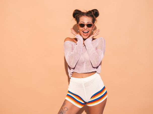 Portrait of young beautiful sexy woman with two horns hairstyle. Trendy girl in casual summer hipster knitted cardigan topic ,shorts in sunglasses. Shocked and surprised with hands near face - Photo, image