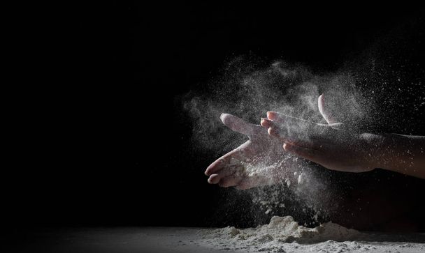 woman chef hand clap with splash of white flour and black background with copy space. - Фото, зображення