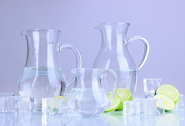 Glass pitchers of water with ice and lime on grey background - Photo, image