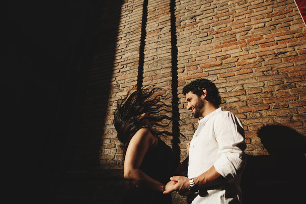 Casal amoroso desfrutando de um passeio na cidade. Atrás deles está o fundo é uma parede de tijolo vermelho
 - Foto, Imagem