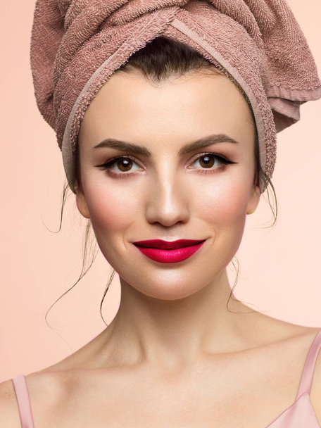 Beauty close-up with evening make-up makeup. Pure, radiant skin of the face, a towel on his head and a slight playful smile. Spa treatments and beauty care. Red lips and black arrows on the eyes. - Foto, imagen