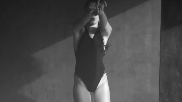 Gri beton duvarlar ile puslu stüdyoda dans siyah vücut takım elbise güzel şehvetli kadın - siyah ve beyaz video - Video, Çekim