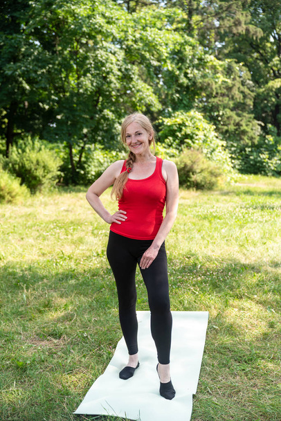 Middle aged woman preparing for practice yoga mat in a park. - Foto, Imagem
