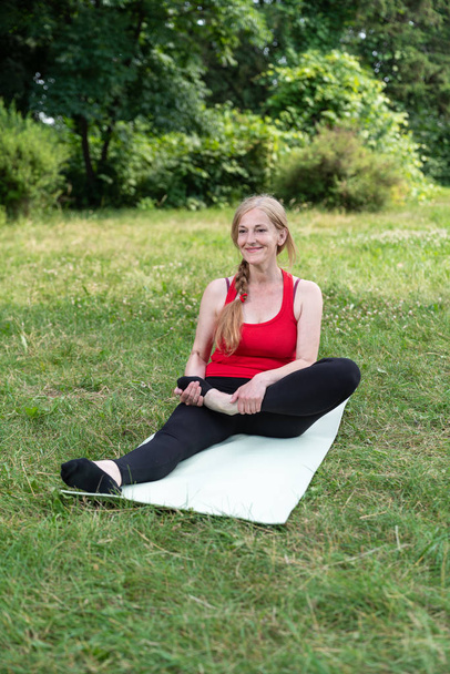 La mejor anciana practica yoga en un parque con top rojo. Mujer feliz haciendo ejercicios al aire libre y sonriendo
 - Foto, imagen