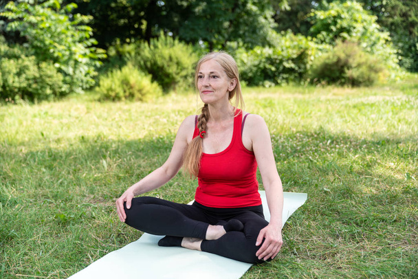 bestbetagte Dame meditiert in einem Park auf einem Gras. - Foto, Bild