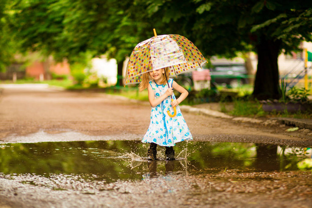 щаслива дівчинка в одязі з парасолькою і гумовими черевиками в калюжі на літній прогулянці
 - Фото, зображення