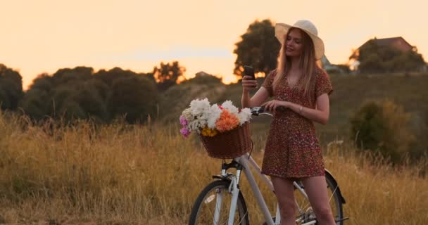 Mooi schattig meisje met behulp van smartphone naast haar fiets in het park met palmen op een zonnige dag. Mooi meisje met smartphone naast haar fiets in het Park op een zonnige dag. - Video