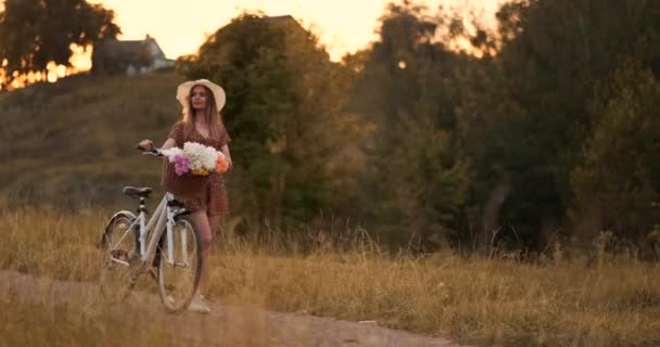 Joven hermosa chica rubia en verano en vestido y sombrero caminando por la carretera con bicicleta y flores en cámara lenta
 - Imágenes, Vídeo