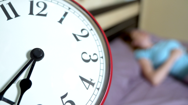 Nahaufnahme des roten Weckers. auf verschwommenem Hintergrund wacht morgens ein Mädchen im blauen Pyjama auf - Filmmaterial, Video