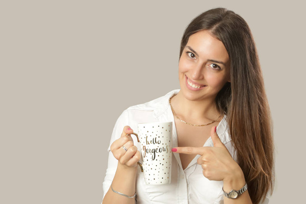 Studio portrait of young smiling brunette pointing the finger to a big mug - Fotografie, Obrázek