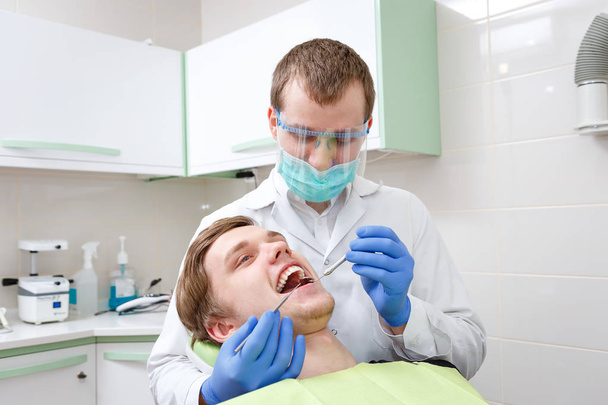 Hombre joven en sillón dentista que tiene dientes examinados en el dentista. Joven dentista masculino
 - Foto, Imagen