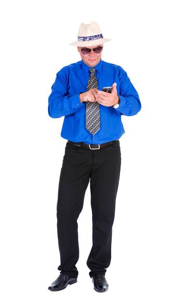 Uomo d'affari serio e concentrato in jeans, camicia blu, cravatta, occhiali da sole e cappello bianco. Leggere e scrivere sms o comporre il numero di telefono sul cellulare smartphone. Isolato sfondo bianco
 - Foto, immagini