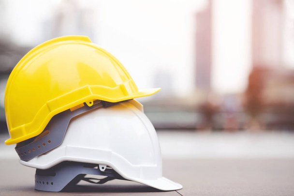 Желтый и белый жесткий защитный шлем носить шляпу в проекте на строительной площадке здания на бетонном полу на город с солнечным светом. шлем для рабочего в качестве инженера или рабочего. концептуальная безопасность
. - Фото, изображение