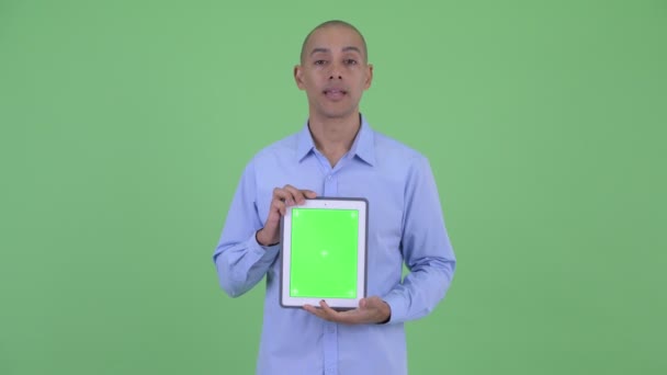Happy bald multi ethnic businessman talking while showing digital tablet - 映像、動画