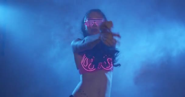 Party sensual woman wearing neon flashing pink bra and glasses dancing in hazy studio nightclub - Footage, Video