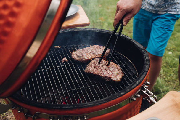 Primo piano maschio mano grigliato succoso pezzo di carne al barbecue alto angolo
 - Foto, immagini