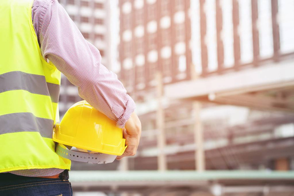 Közelről megtekintéséhez mérnöki férfi építőipari munkás állni gazdaság biztonsági fehér sisak és kopás fényvisszaverő öltözetet a biztonságát a munka működését. szabadtéri épületháttér. - Fotó, kép