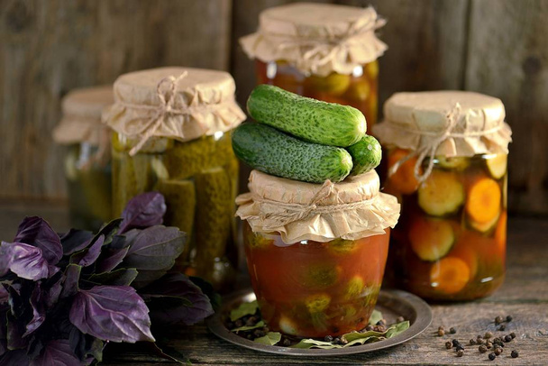 Different pickled cucumbers - whole and slices with onions, carrots in tomato juice on an old wooden background. - Photo, Image