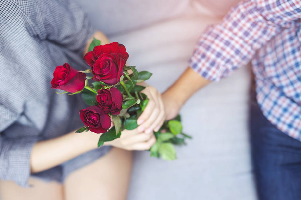 pareja amantes joven hombre sentado en sofá sostiene Bouquet de hermosa una flor de rosa roja en la mano sorpresa dada a la novia felicidad Amor en la Primera Introducido de Relación. Concepto de San Valentín
. - Foto, Imagen