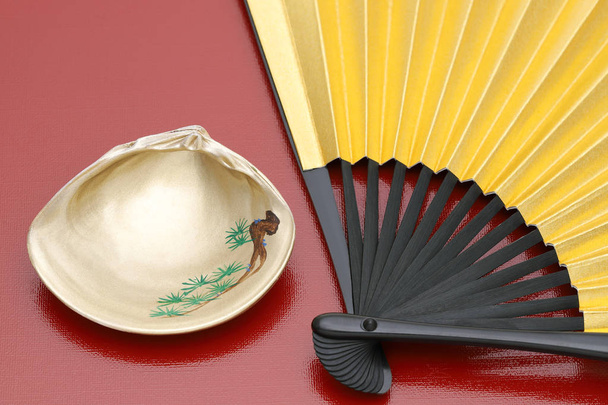 Abanico plegable dorado japonés y concha dorada sobre fondo rojo
 - Foto, imagen