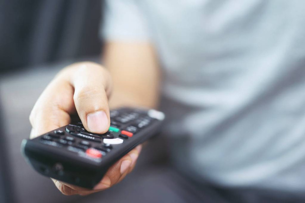Zamknij TV pilot zdalnego sterowania w przypadkowych rękach człowieka wskazując na telewizor i włączyć lub wyłączyć. wybierz kanał oglądania telewizji na kanapie w domu w salonie relaks. - Zdjęcie, obraz