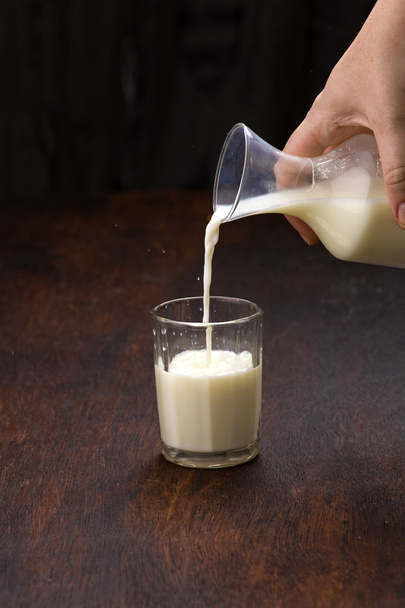 Pouring milk to glass on wooden background - Photo, Image
